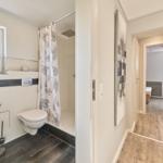 Badezimmer mit Dusche und Toilette. Flur führt in Schlafzimmer.