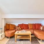 Ein Wohnzimmer mit orangefarbenem Sofa, Holztisch und Teppich.