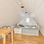 Zimmer mit Bett, Tisch und Stühlen unter schrägen Wänden.