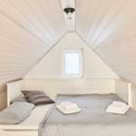 Schlafzimmer mit Dachschrägen, weißer Holzwand und Fenster mit Jalousie.