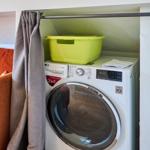 Waschmaschine mit Trocknerfunktion neben einem Sofa mit Kissen.