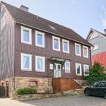 Haus mit braunem Holzschindeldach und Steinsockel. Vorhof mit gepflastertem Parkplatz.