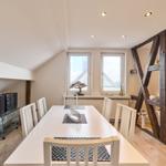 Esszimmer mit weißem Tisch, Stühlen und Holzbalken. Fenster und Holzboden sichtbar.