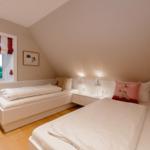 Zwei Einzelbetten in einem Dachzimmer mit Fenster und Nachttischen.