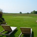 Zwei Liegestühle auf grünem Rasen mit Blick auf Feld und Himmel.