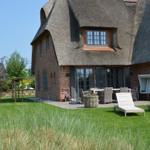 Haus mit Strohdach, Terrasse, Liegestühle und Garten.