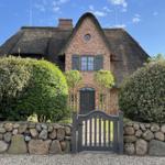 Rotes Backsteingebäude mit Strohdach, Eingangstor und Steinmauer.