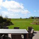 Terrasse mit Tisch und Stühlen, Blick auf grünes Feld und Himmel.