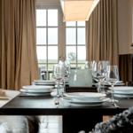 Esstisch mit Geschirr und Gläsern vor Fenster mit Blick auf Landschaft.