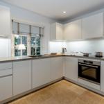 Moderne Küche mit weißen Schränken, Edelstahlgeräten und Blick auf Garten.