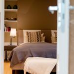 Schlafzimmer mit Bett, Kissen und Nachttisch. Hintergrundregal mit Büchern und Dekorationsgegenständen.