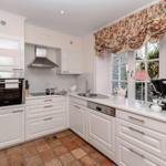 Küche mit weißen Schränken, Herd, Spüle und Fenster mit Vorhang.