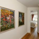 Flur mit zwei Gemälden und Blick in Schlafzimmer mit Bett und Fenster.