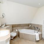 Badezimmer mit Badewanne, Waschbecken und Toilette. Weiße Wände und Fliesen.