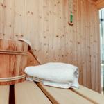 Sauna mit Holzbank, Eimer und Handtuch. Im Hintergrund Bad mit Dusche.