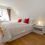 Schlafzimmer mit Bett, Nachttisch und Fenster mit Vorhängen.