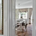 Esszimmer mit Tisch, Stühlen und Kronleuchter. Terrasse über französische Tür. Fliesenboden und Spiegel an der Wand.