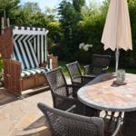 Garten mit Liegestuhl, Tisch und Stühlen, Sonnenschirm und Blumen.