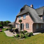 Rotes Backsteingebäude mit Strohdach, Garten mit Terrasse und Sitzgelegenheiten.