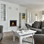 Wohnzimmer mit Kamin, Sofa und Couchtisch. Bücherregal und Fenster sichtbar.