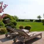 Zwei Liegestühle auf Steinplatten mit Blick auf grünen Rasen und blühenden Baum.