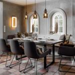 Esszimmer mit Tisch, Stühlen und Bänken unter Bogenfenstern.