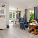 Wohn- und Essbereich mit Sofa, Stuhl und Esstisch. Holzboden und große Fenster.