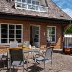 Terrasse mit Sitzgruppe, Gazebo und Gartenhaus vor einem Backsteinhaus.