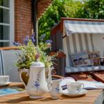 Holztisch mit Teeservice, Blumen und Strandkorb im Garten.