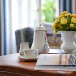 Holztisch mit Teeservice, Blumen und Zeitschriften vor Fenster mit Vorhängen.