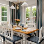 Esszimmer mit Holztisch, weißen Stühlen und blauen Gardinen.
