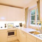 Küche mit weißen Schränken, Spüle und Fenster mit Vorhängen.