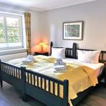 Schlafzimmer mit Bett, Nachttischen und Fenster. Gelbe Bettwäsche und karierte Vorhänge.