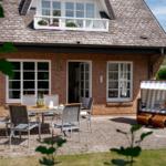 Haus mit Terrasse, Gartenmöbeln und Strandkorb.