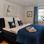 Schlafzimmer mit Bett, Kissen und Frühstückstablett. Fenster mit Vorhängen und Wandbild.