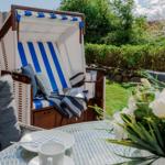 Terrasse mit Strandkorb, Tisch und Blumen. Hintergrund: grüner Garten.