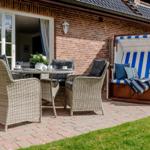 Terrasse mit Sitzgruppe und Strandkorb. Roter Kies und grüner Rasen.