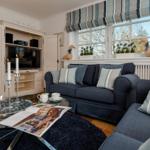 Ein Wohnzimmer mit Sofa, Fernseher und Fenster mit Blick auf den Garten.