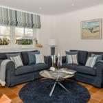 Ein Wohnzimmer mit zwei dunkelblauen Sofas, runden Teppich und Glas-Tisch.