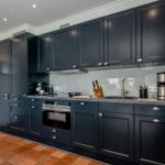 Küche mit dunklen Schränken, Edelstahlgeräten und Terrakottaboden.