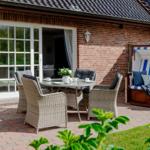 Terrasse mit Sitzgruppe, Strandkorb und Gartentisch. Blick ins Haus durch Fenster.