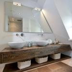Badezimmer mit Holzwaschtisch, zwei Waschbecken und Spiegel unter Dachschrägen.