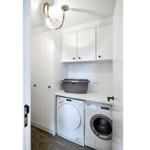 Wäscherei mit Waschmaschine und Trockner, weiße Schränke und grauer Wäschekorb.