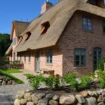 Rotes Backsteinhaus mit strohgedecktem Dach und grüner Umgebung.