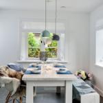 Esszimmer mit weißem Tisch, Stühlen und Fenstern. Blaue Tischdecken und Blumen auf dem Tisch.