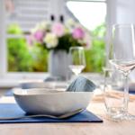 Tisch mit Teller, Gläsern und Blumenvase vor Fenster