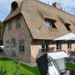 Haus mit Strohdach, Terrasse mit Sonnenschirm und Liegestühlen im Garten.