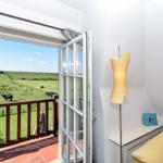 Durch offene Tür Blick auf grünes Feld mit Kühen und Balkon mit roten Fliesen.