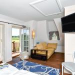 Schlafzimmer mit Sofa, Fernseher und Balkonblick auf grüne Landschaft.