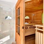 Dusche mit Glaswand und Sauna mit Holzbank und Dampfstein.